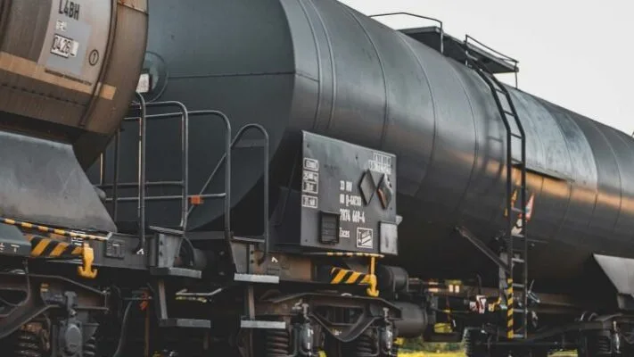 Black industrial railway tanker car with hazard markings and access ladder on tracks.