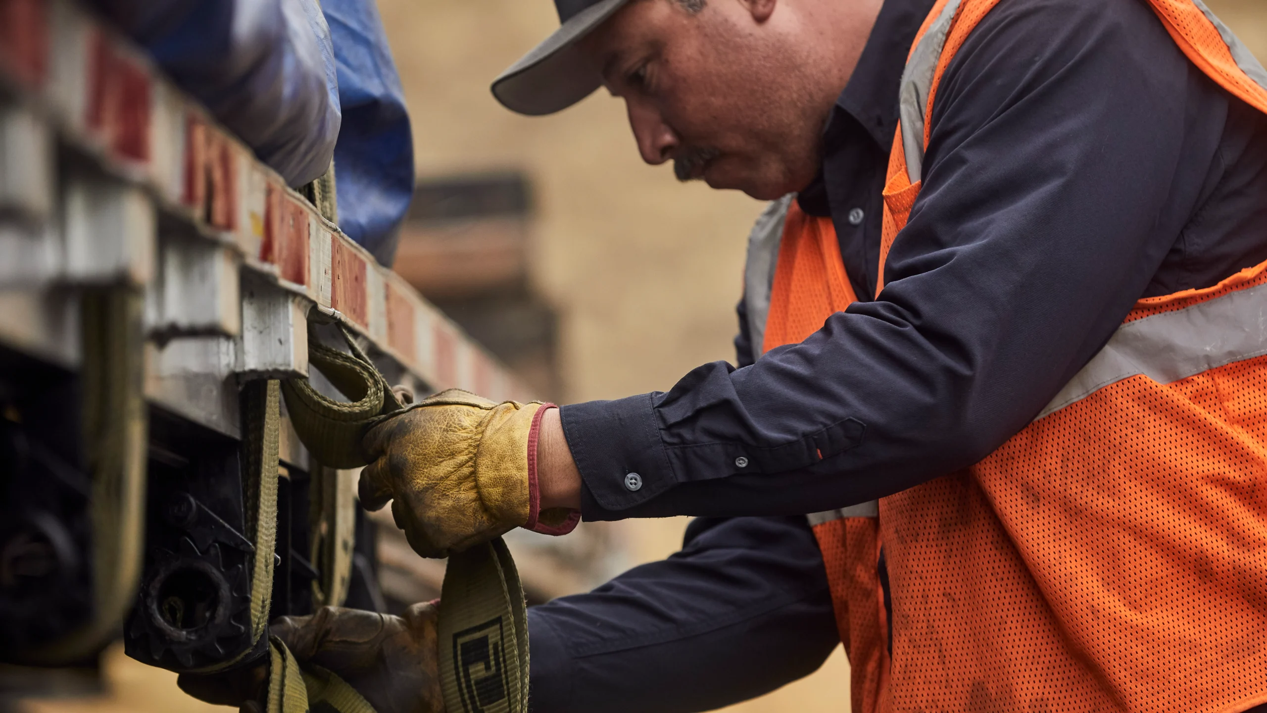 Construction worker in orange safety vest and work gloves securing straps on equipment at a job site.